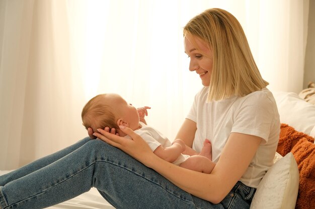 Mama hält ein neugeborenes Baby in ihren Armen, im Hintergrund scheint die Sonne aus dem Fenster