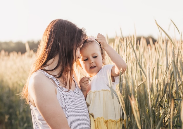 Mama hält ihre kleine Tochter im Sommer auf einem Weizenfeld im Arm