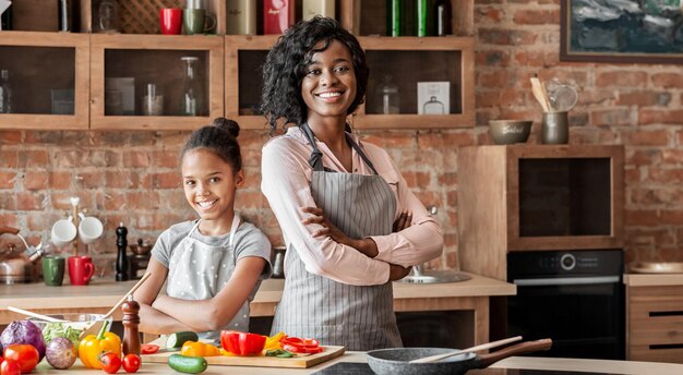 Mamá y hija confiadas posando para la cámara mientras cocinan