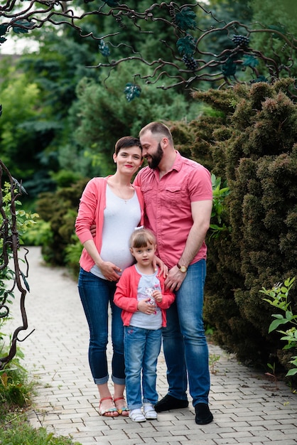 Mamá, hija y papá embarazadas están caminando en el parque.