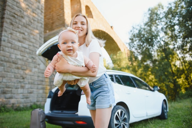 Foto mamá con hija pequeña en la naturaleza cerca del coche.