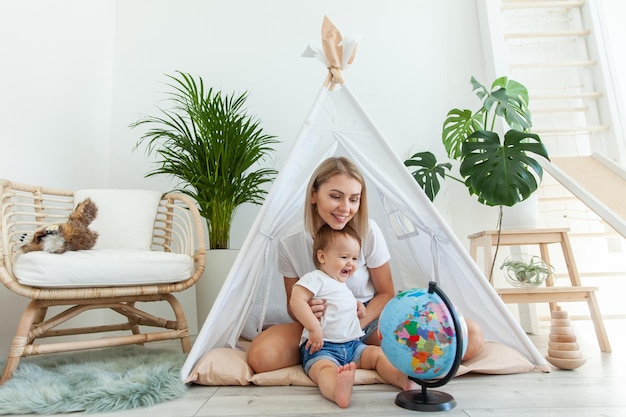 Mamá con una hija pequeña sentada en un wigwam en casa estudiando el globo pasar tiempo juntos concepto de Matyrdom