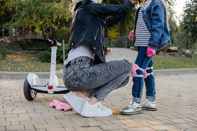 Mama hilft dabei, die Ausrüstung und den Helm ihrer kleinen Tochter für eine Segway-Fahrt im Park anzuziehen