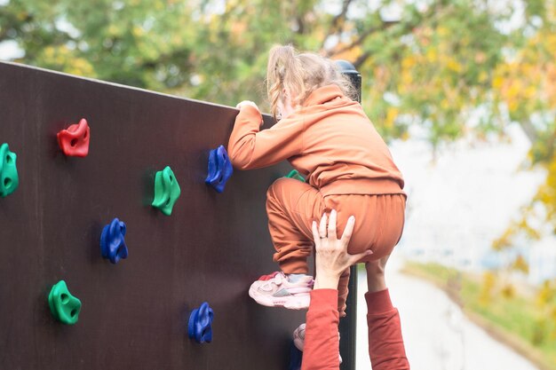 Mama hilft ihrer kleinen Tochter, das künstliche Bergrelief an der Straßenmauer zu überwinden