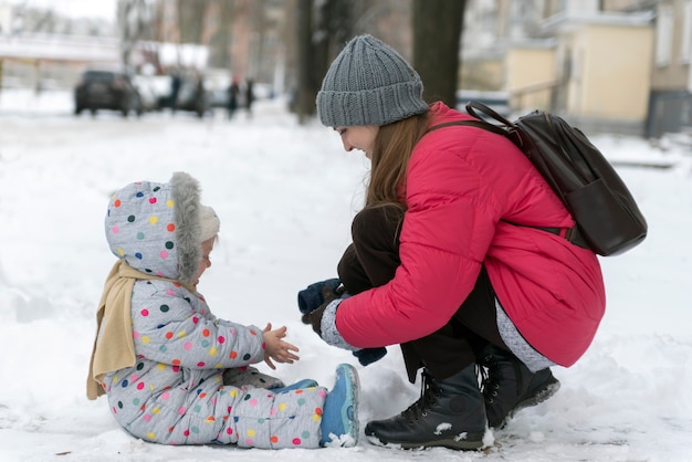 Mama hilft ihrer Tochter, einen Fäustling anzuziehen, den ersten Schnee. Winterspaziergang.