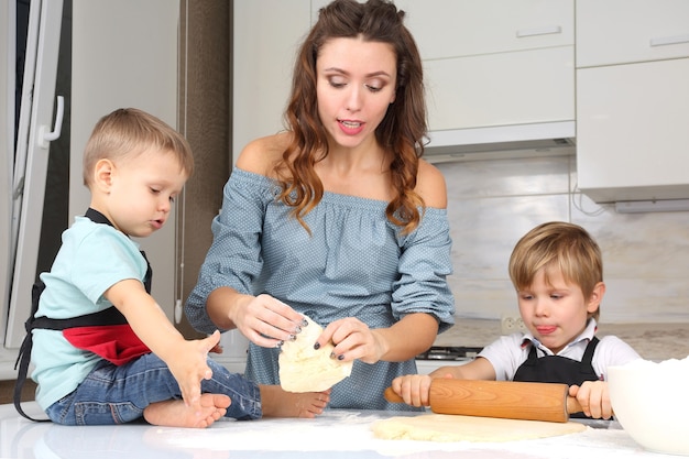 Mama hilft jungen Söhnen, den Teig auf dem Küchentisch zu kneten