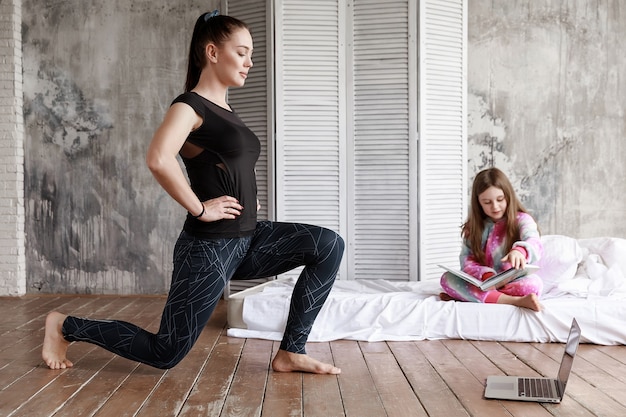 Mama ist zu Hause sportlich aktiv, hundert Online-Lektionen, und meine Tochter sitzt neben ihr und liest ein Buch