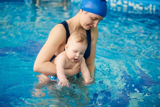 Mamá joven desarrolla los músculos del bebé Haciendo varios ejercicios en la piscina Tratamientos de agua desde los primeros días de vida de los bebés