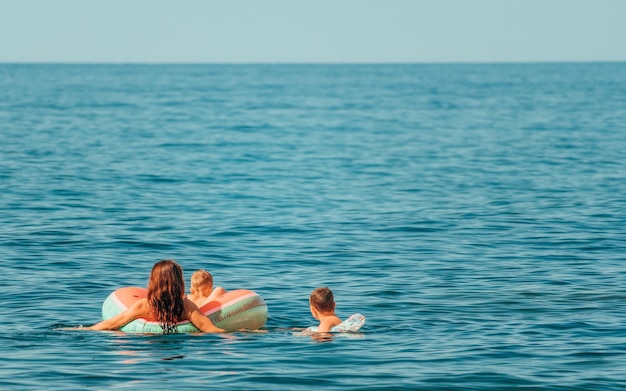 Mamá joven y dos niños nadando en el mar azul mujer delgada en bikini e hijo pequeño con inflable