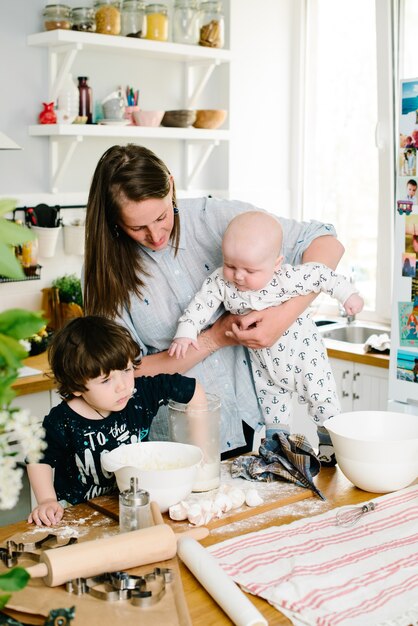 Mamá joven y feliz con sus hijos en la cocina cocinar masa para galletas o pastel