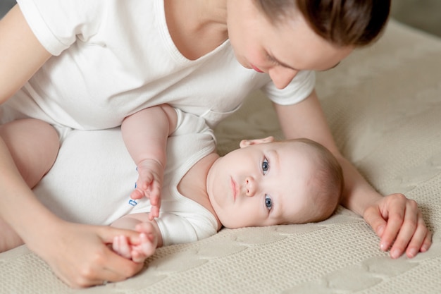 Mamá juega con el bebé 6 meses en la cama en casa