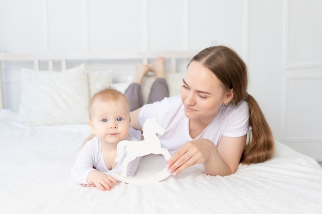 Mamá juega con bebé caballo de juguete de madera en la cama en casa, familia feliz