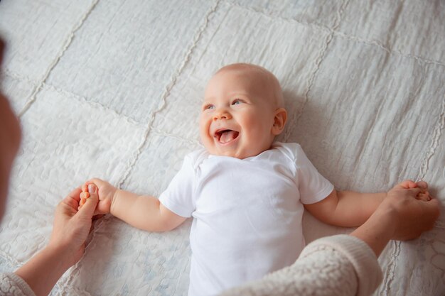 Mamá juega con el bebé, le da un masaje y controla su cuerpo. Niño con un traje blanco.