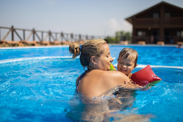 Mamá juega con su hijo con mangas en la piscina en verano