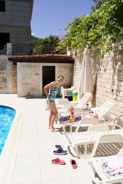 Mamá se para junto a una niña sentada en una tumbona junto a la piscina