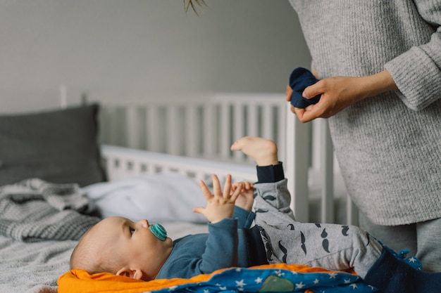 Mama kleidet den süßen kleinen Jungen in einen Overall. Glückliche junge Mutter, die mit Baby auf Bett spielt. Glückliche Mutterschaft. Säuglingsbaby.