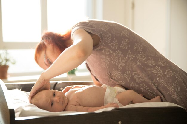 Mama kümmert sich um ihr kleines Baby, das auf einem Bett liegt