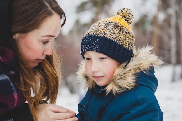 Mama küsst und wärmt die Hände ihres kleinen Sohnes, geht im Winterpark spazieren, geht, kalt, friert die Hände