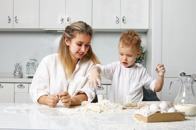 Mama lächelt, als sie sieht, wie ihr Sohn in einer weißen Küche fleißig aus Mehl und Teig zubereitet wird