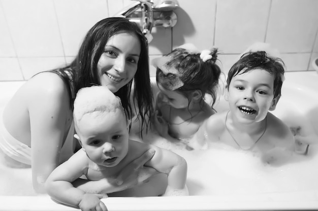Mamá lava a los niños Mamá y niños están tomando procedimientos de agua en el baño Spray de espuma