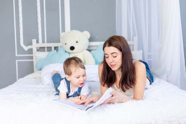 Mamá lee un libro al niño o le enseña en casa en la cama Familia cariñosa feliz. Mamá e hijo