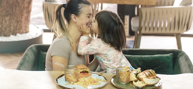 Foto mamá con una linda hija comiendo comida rápida en un café