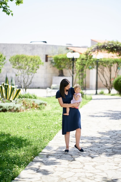 Mamá lleva a una niña por el camino en el parque.