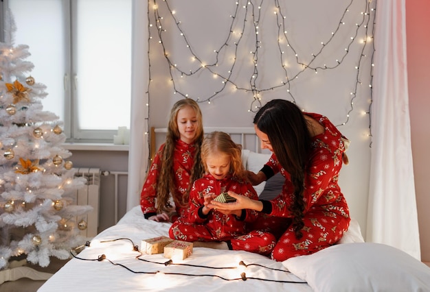 Mama macht ihrer Tochter ein Weihnachtsgeschenk. Glückliche Familie im roten Weihnachtspyjama im Schlafzimmer am Weihnachtsmorgen. Neujahr