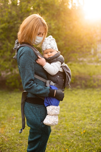 Mamá con máscara médica e hijo pequeño en un paseo por la naturaleza en el parque de primavera al atardecer