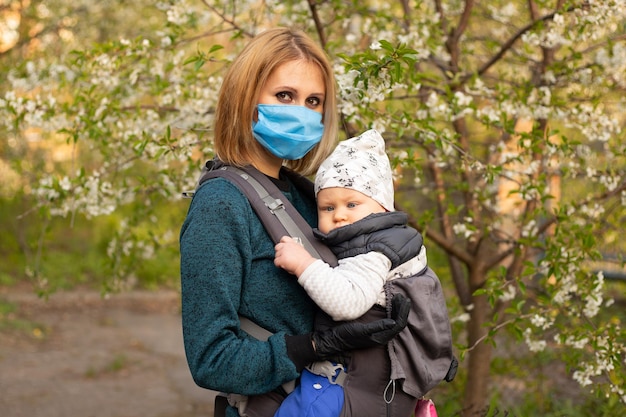 Mamá con máscara médica e hijo pequeño en un paseo por la naturaleza en el parque de primavera