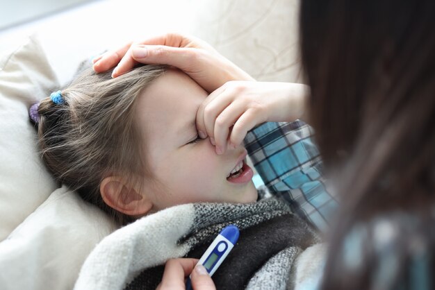 Mamá midiendo la temperatura de la niña enferma con termómetro