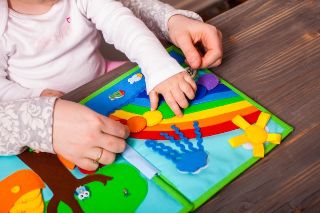 Mama mit Baby skizziert die Farben des Regenbogens in einem farbigen Buch aus Filzmaterial, handgefertigt