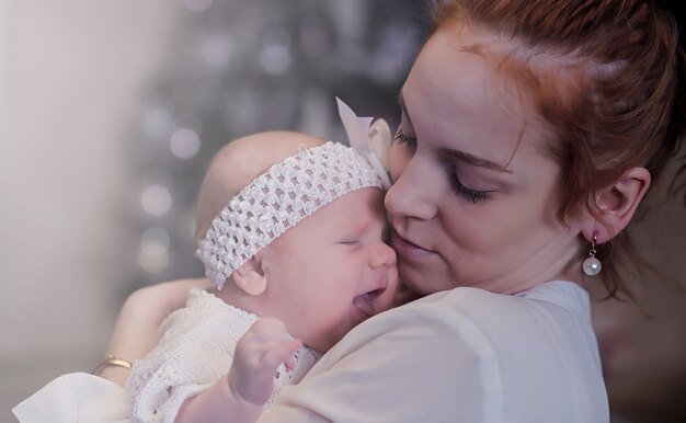 Mama mit einem neugeborenen Baby im Arm. Das Mädchen hält ein Baby vor dem Fenster. Neugeborenes auf Mutterhänden.