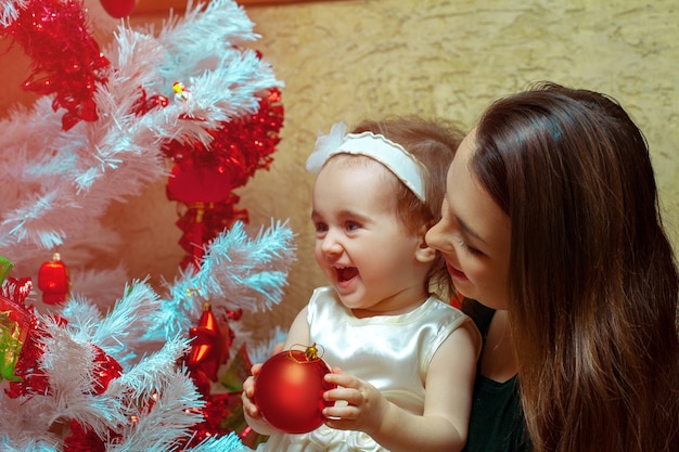 Mama mit einer kleinen Tochter schmücken einen Weihnachtsbaum und haben Spaß