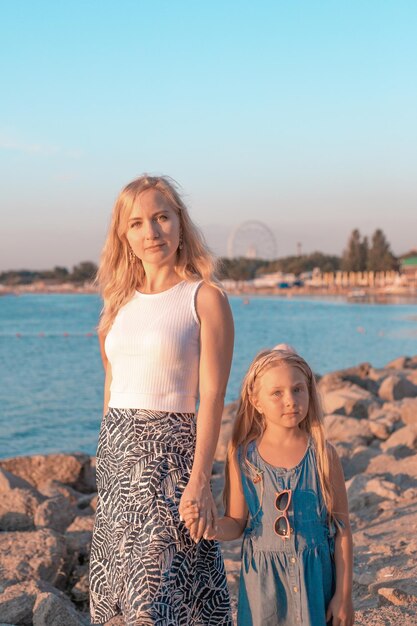 Mama mit ihrer blonden Tochter am Strand bei Sonnenuntergang. Sommerruhe und Unterhaltung.