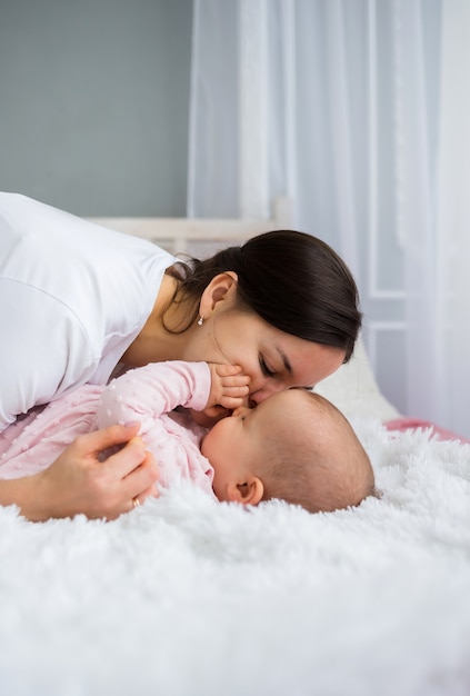 Mamá morena besa a su hija en la cama de la habitación