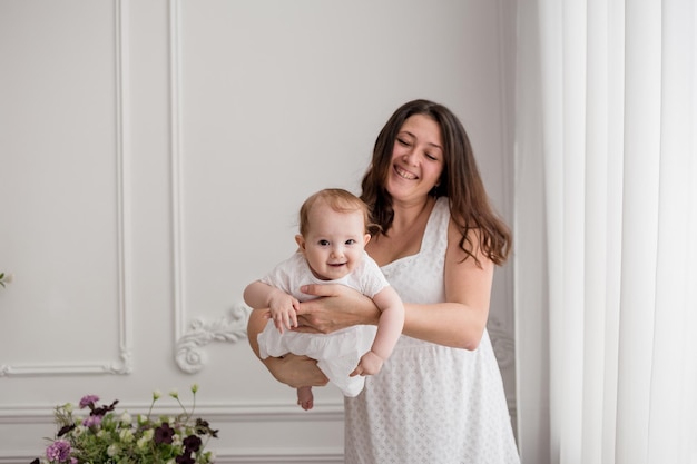 Mamá morena caucásica está jugando con su hija en una habitación blanca Tiempo feliz con mamá