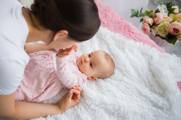 Mamá morena juega con su hija en un vestido rosa en la cama