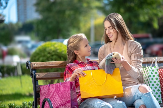 Mamá mostrando a su hija nueva bufanda, sentada en un banco del parque