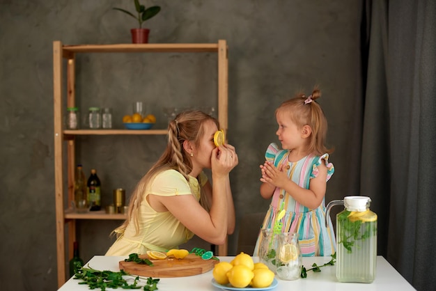 Mamá muestra rodajas de limón en lugar de ojos y juega con su hija en la cocina