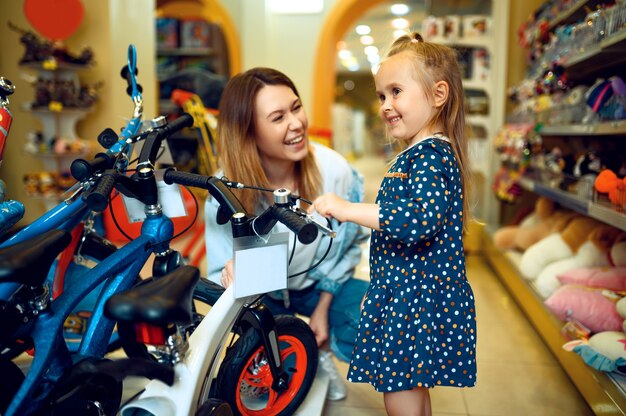 Mamá y niña bonita eligiendo bicicleta en la tienda del niño