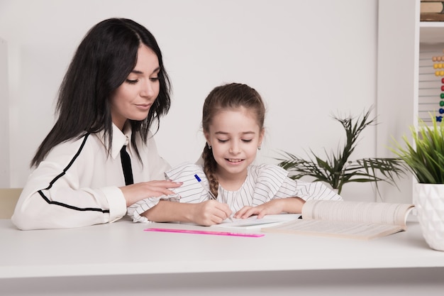 Mamá con niña juntos en casa sentados a la mesa.