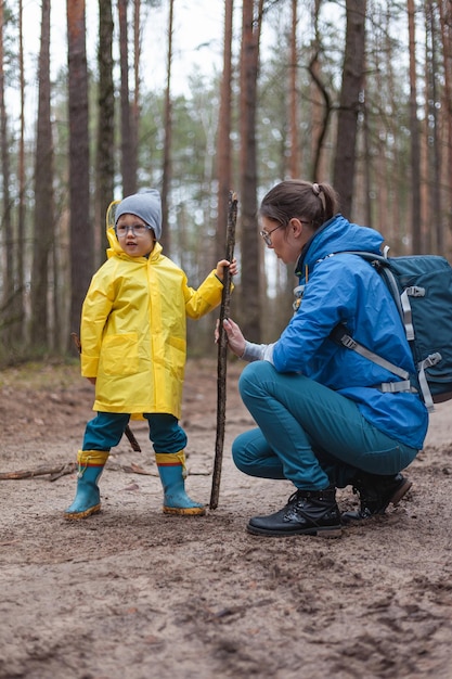 Mamá y niño caminan juntos en el camino del bosque después de la lluvia en impermeables