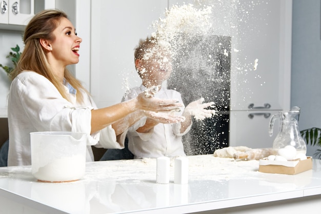 Mamá y niño en la cocina blanca tiran harina al aire y se regocijan