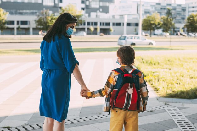 Mamá con un niño enmascarado ir a la escuela o jardín de infantes