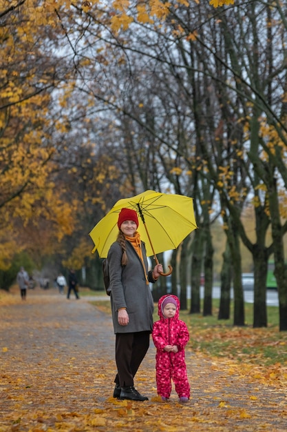 Mamá y niño están parados bajo una sombrilla en un parque de otoño. Marco vertical.