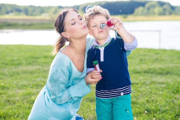 Mamá con niño haciendo burbujas en el parque en un día soleado de verano