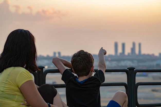 Mamá y niño mirando la vista del horizonte de la ciudad de Madrid al atardecer. Niño señalando la silueta de las 4 torres