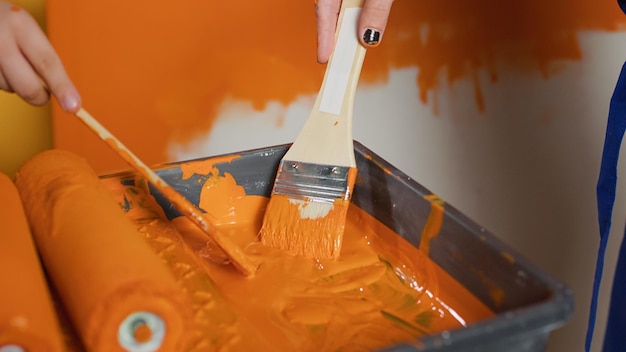 Mamá y niño pintando paredes con color naranja y pincel, usando herramientas de bricolaje renovadoras en casa. Personas que trabajan en la mejora de la redecoración con pintura y equipo. De cerca.