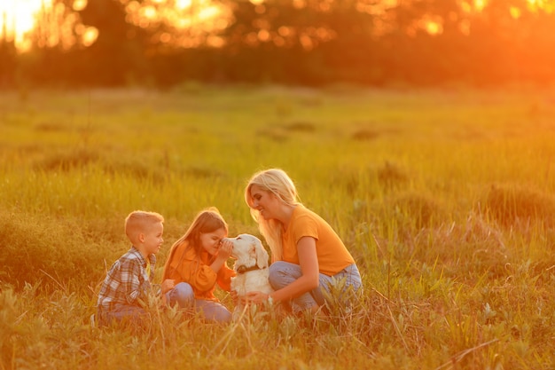 Mamá con niños al atardecer caminando con un perro perdiguero de mascotas al aire libre